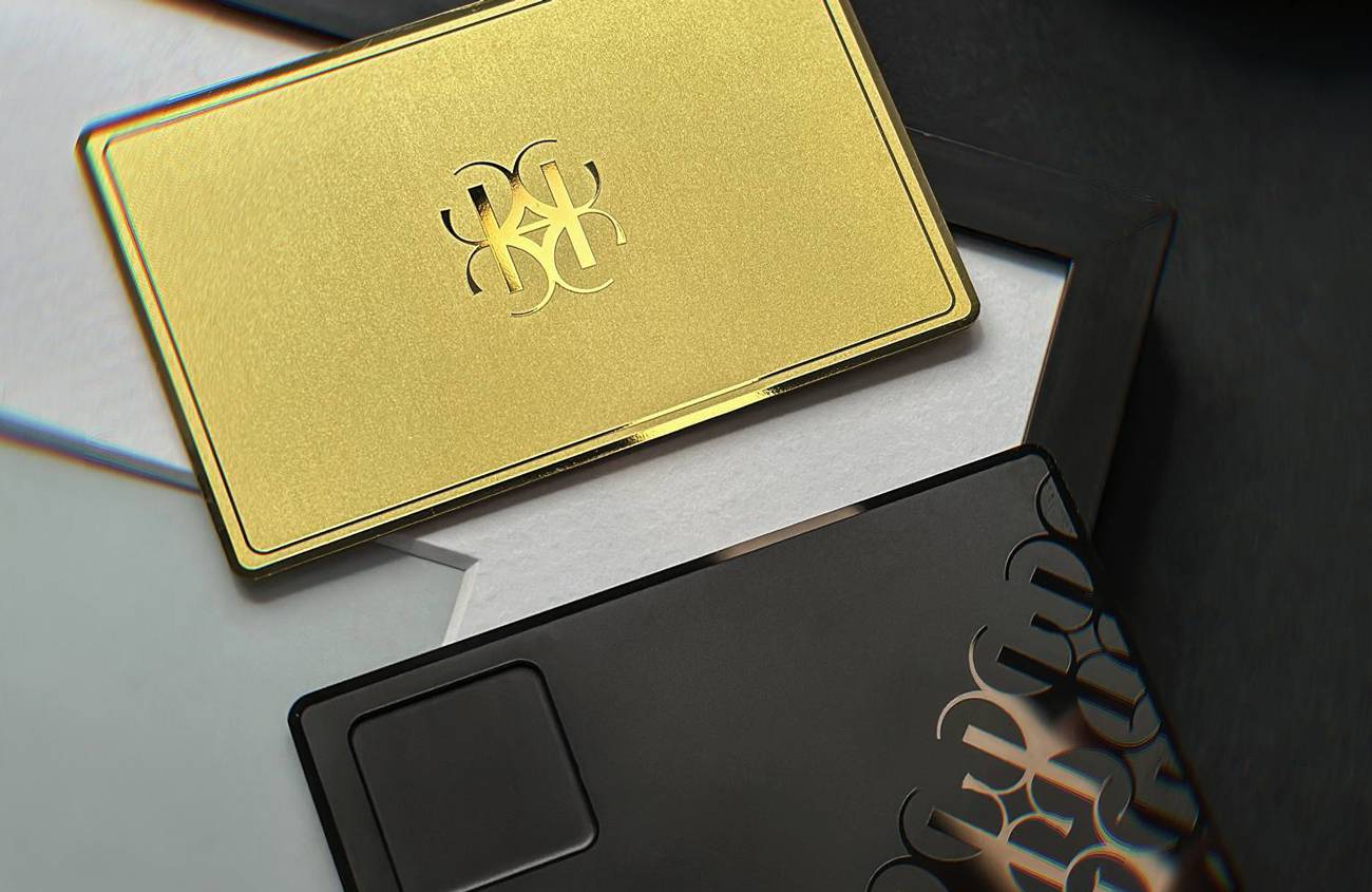 Zelta metāla vizītkarte ar gravētu monogrammu blakus melnam maciņam