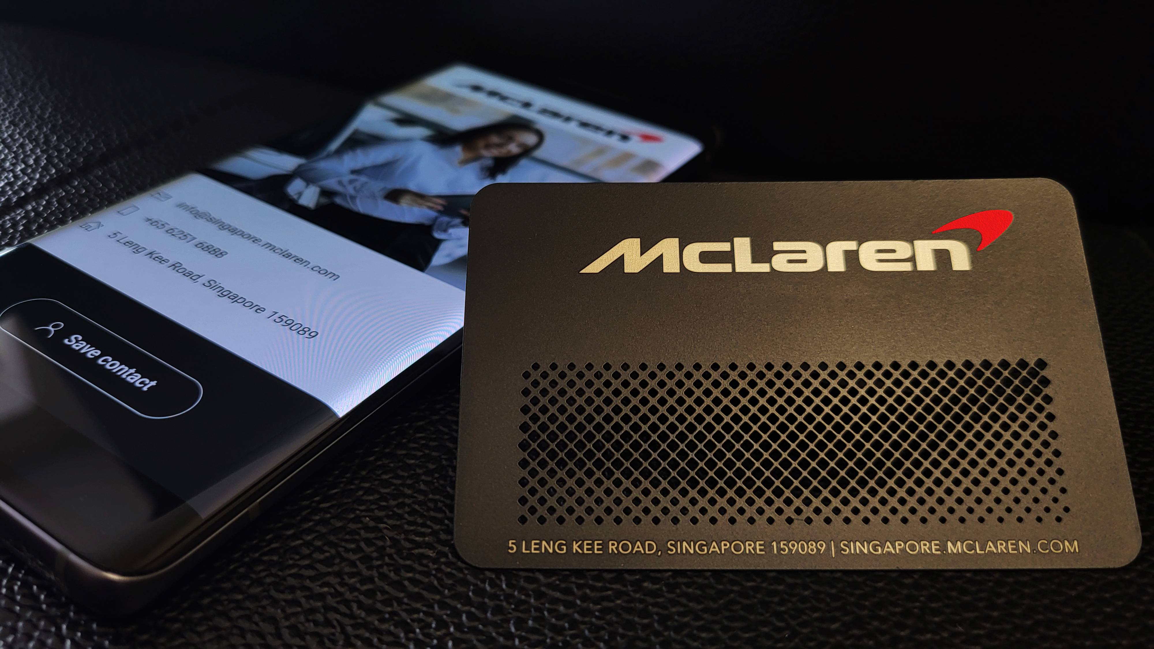 McLaren metāla vizītkarte ar perforāciju blakus tālrunim ar digitālo profilu