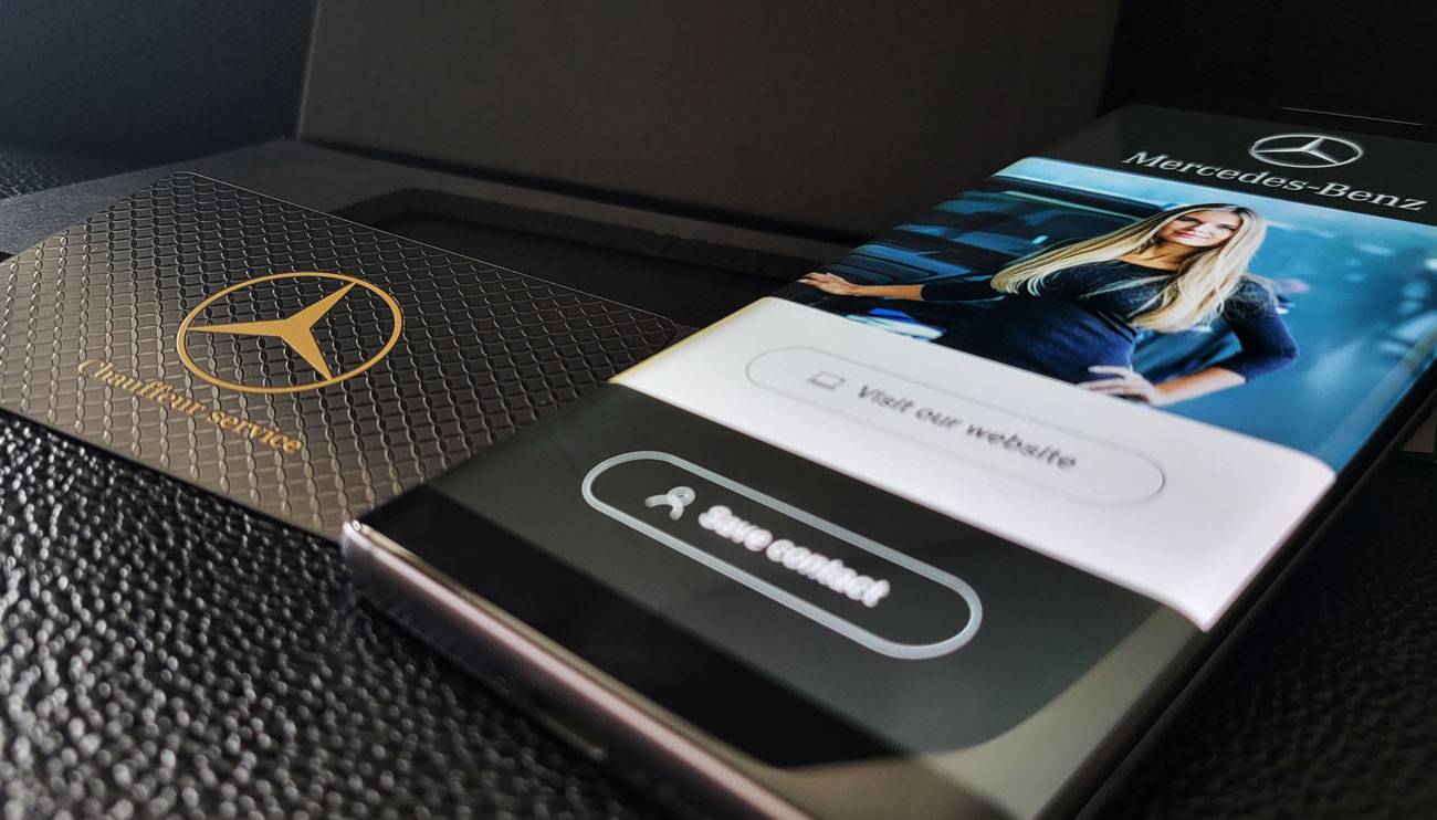 Melna Mercedes-Benz metāla vizītkarte blakus tālrunim ar digitālo profilu