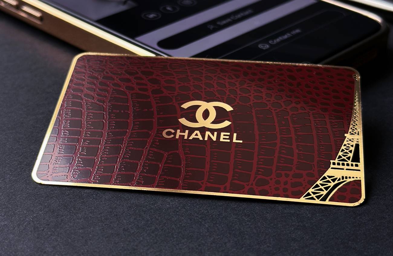 Bordo un zelta Chanel metāla vizītkarte ar gravētu rakstu blakus tālrunim