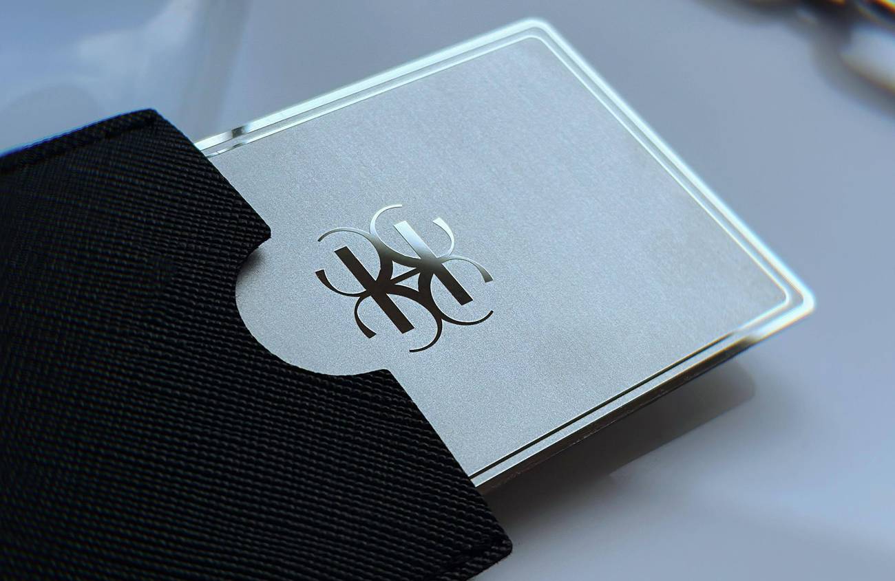 Spoguļspīdīga sudraba metāla vizītkarte ar gravētu monogrammu un melnu maciņu
